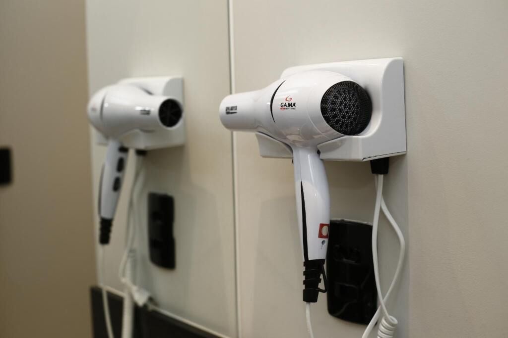 Dos secadores de pelo fijos a la pared, con cables conectados a enchufes.