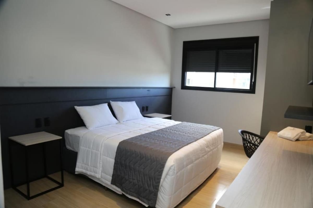 Un dormitorio moderno con cama, mesitas de noche, una ventana y un escritorio.