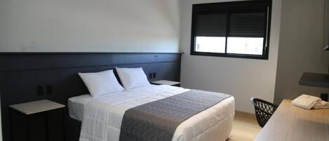 A modern bedroom with a bed, bedside tables, a window, and a desk.