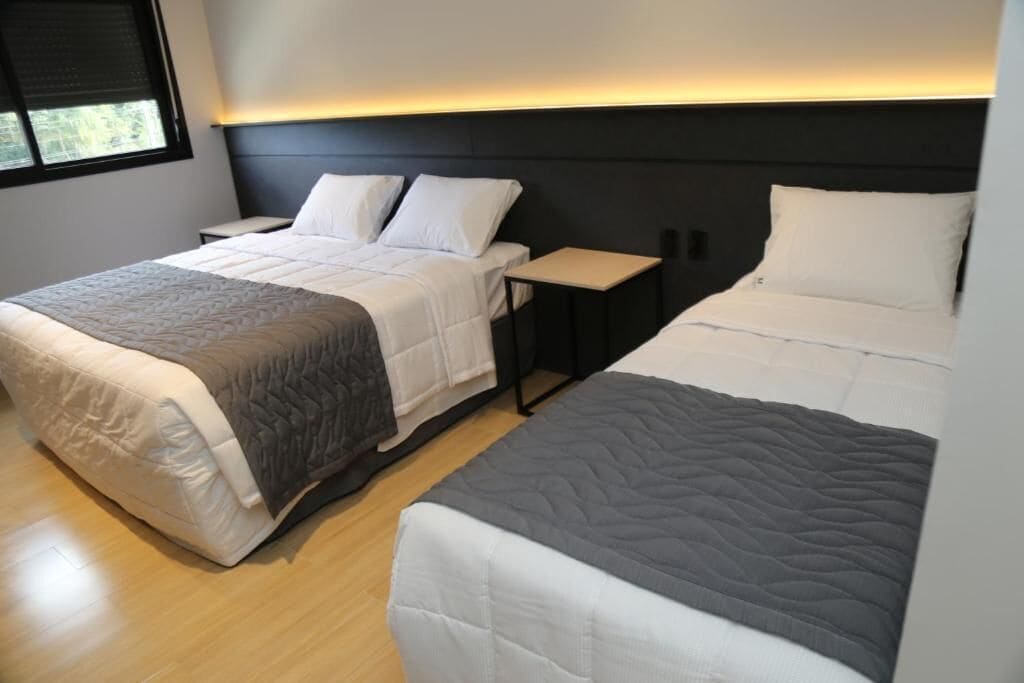 A hotel room with two beds, a bedside table, and a window.