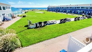 A hotel with a well-maintained lawn, outdoor seating area, and a view of the ocean. - Edgewater Beach Resort (Dennis Port)