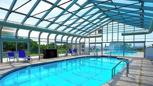 A large indoor swimming pool with a glass ceiling, surrounded by blue chairs and a poolside area. - Edgewater Beach Resort (Dennis Port)