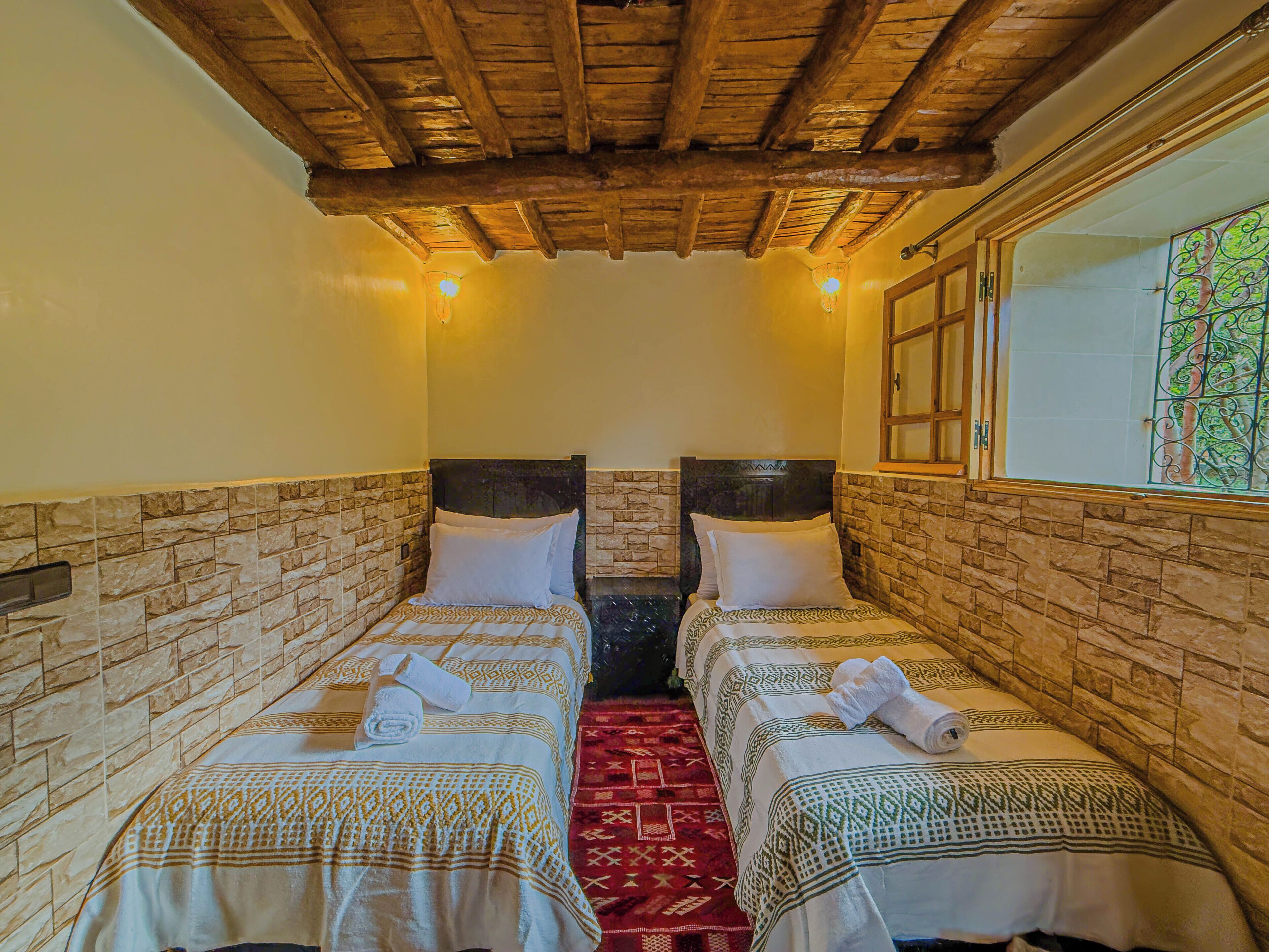 A room with two beds, each with a patterned bedspread and pillows, a red carpet, and a wooden ceiling.