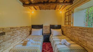 A room with two beds, each with a patterned bedspread and pillows, a red carpet, and a wooden ceiling.