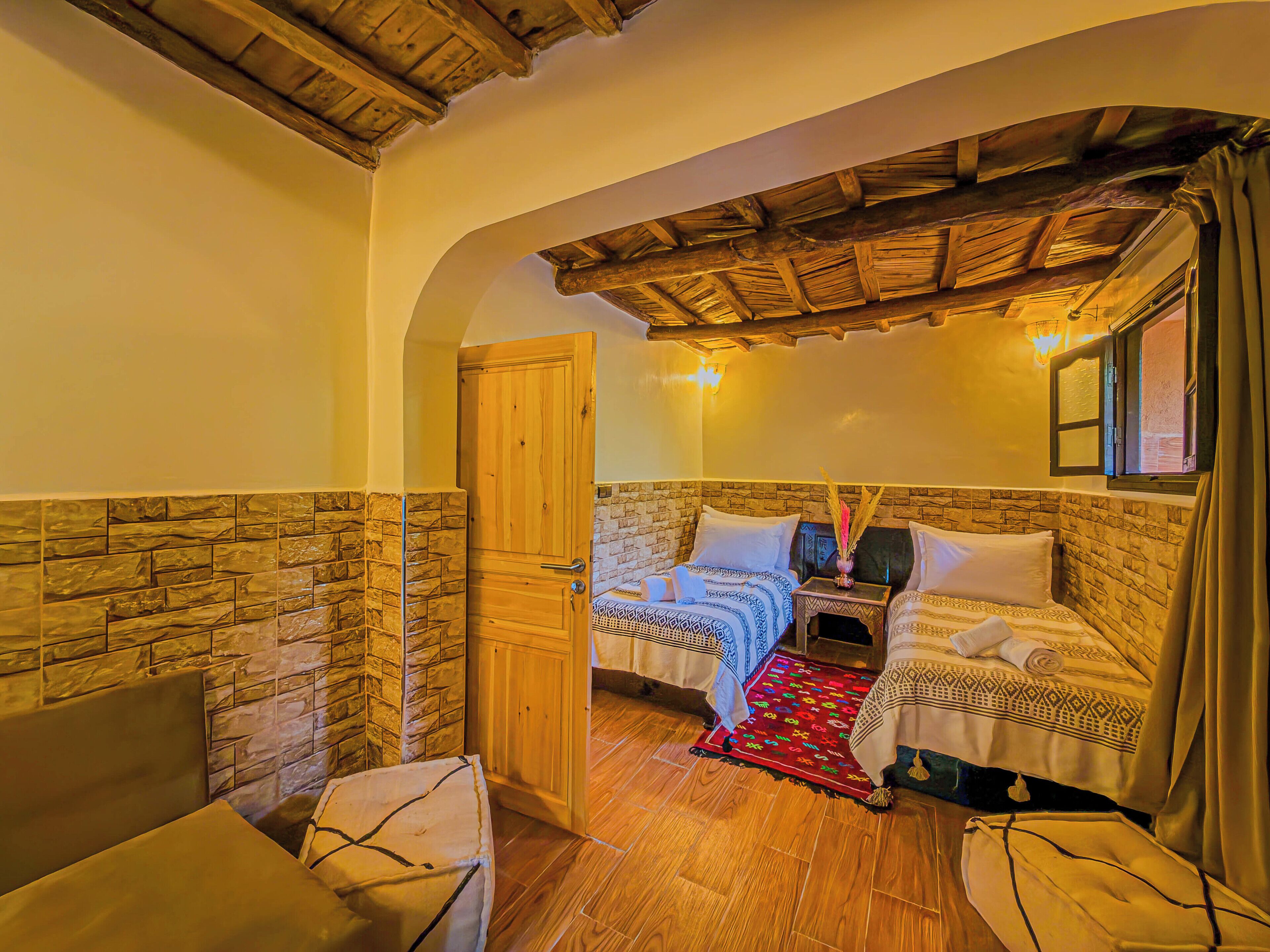 Une pièce avec un mur en pierre, un plafond en bois, un lit avec une literie à motifs, une petite table et une chaise.