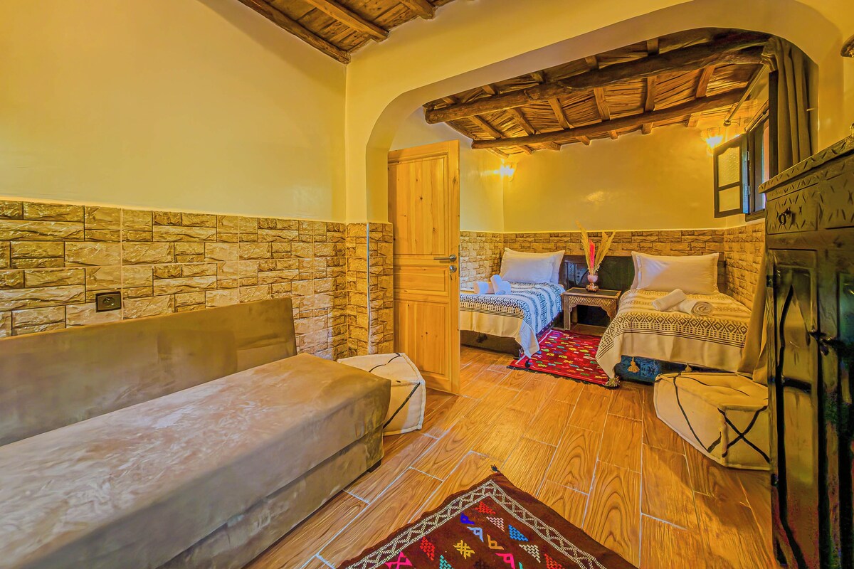 Una habitación con pared de piedra, techo de madera, una cama con edredón estampado, un sofá y una pequeña mesa.