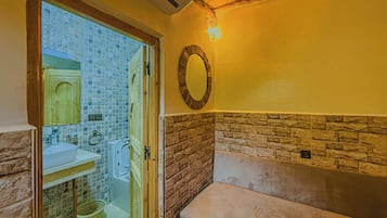 Une salle de bain avec un mur en pierre, un plafond en bois, un miroir rond et une baignoire.