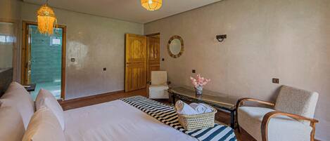 Un dormitorio con una cama grande, una silla, una mesita con un florero y una puerta que da a un baño.