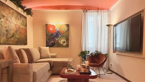 Uma sala de estar com sofá, mesa de centro, uma cadeira, um quadro e uma janela com cortinas.