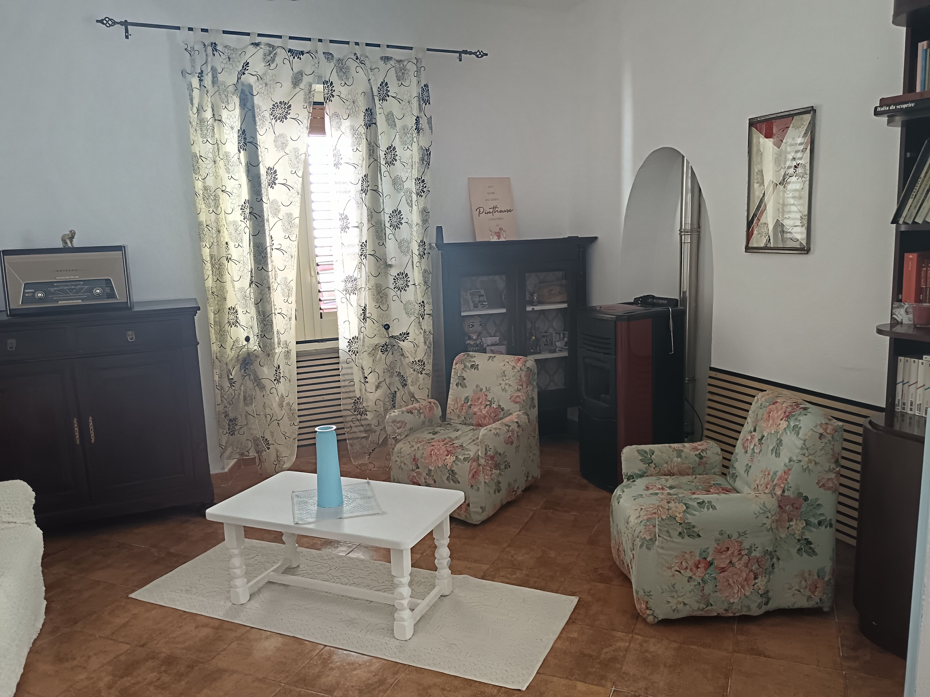 Una sala de estar con una mesa blanca, sillones estampados, una estantería y un radiador.