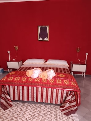 A hotel room with a red wall, a bed with striped bedding, two bedside tables with lamps, and a framed picture on the wall.