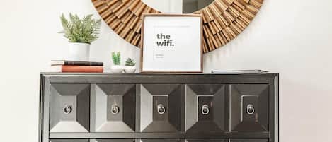Un espejo fijado a la pared con marco de madera, un cartel enmarco que dice 'the wifi', y un mueble decorativo con varios cajones.