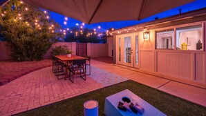 En terrasse med bord og stole, et overdækket siddeområde og en bygning med vinduer og døre.