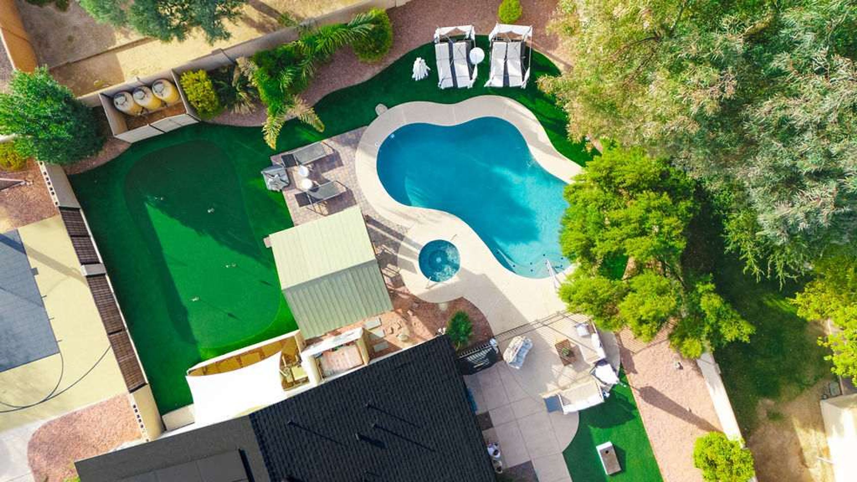 A swimming pool with a unique shape, surrounded by a deck area with lounge chairs and umbrellas.