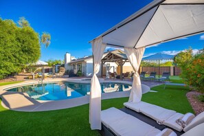Ein Garten mit Swimmingpool, Liegestühlen und einer überdachten Terrasse.