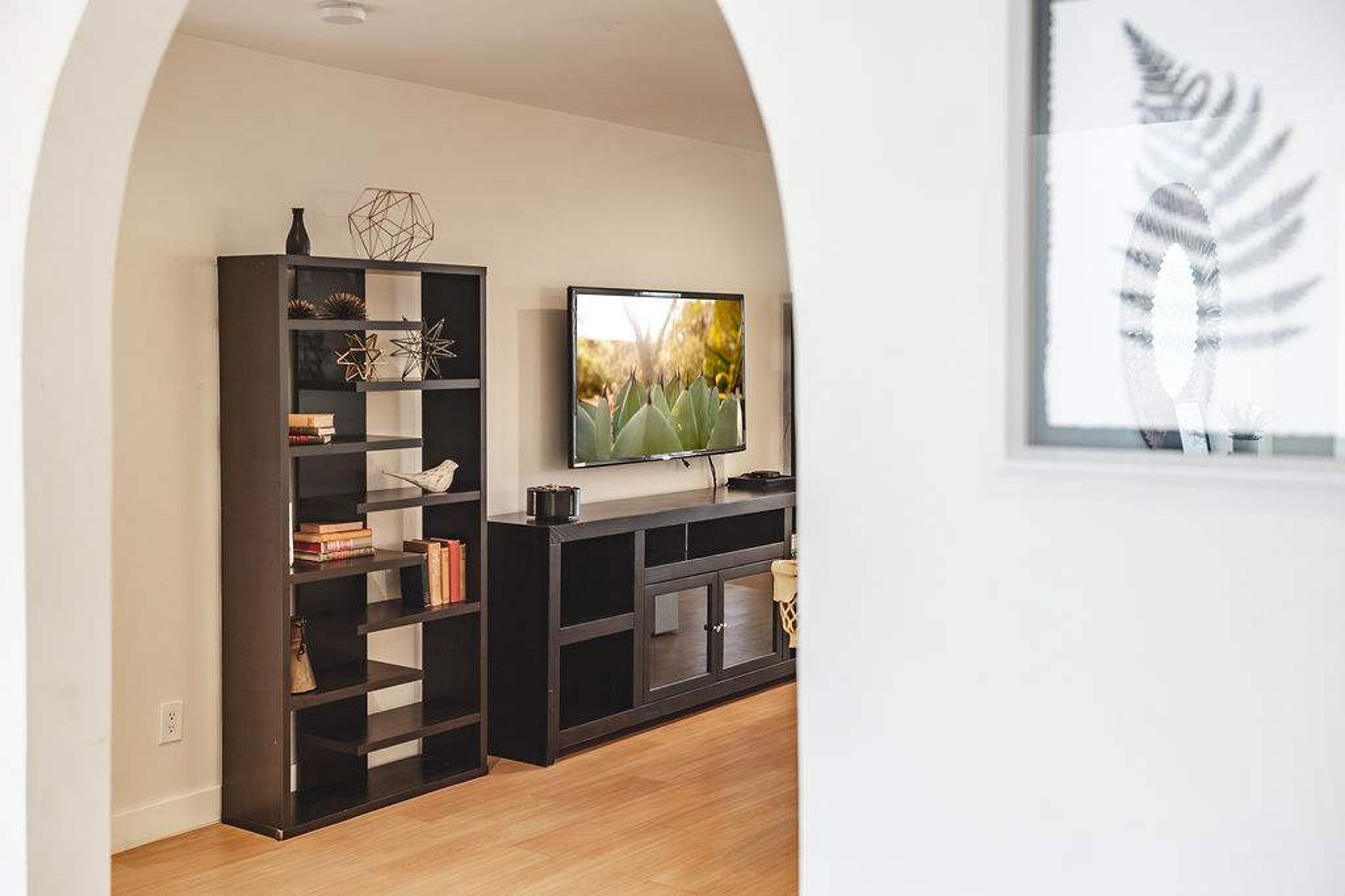 Un salon moderne avec un meuble de rangement en bois foncé pour l’équipement audiovisuel, un téléviseur à écran plat et une estampe botanique encadrée accrochée au mur.