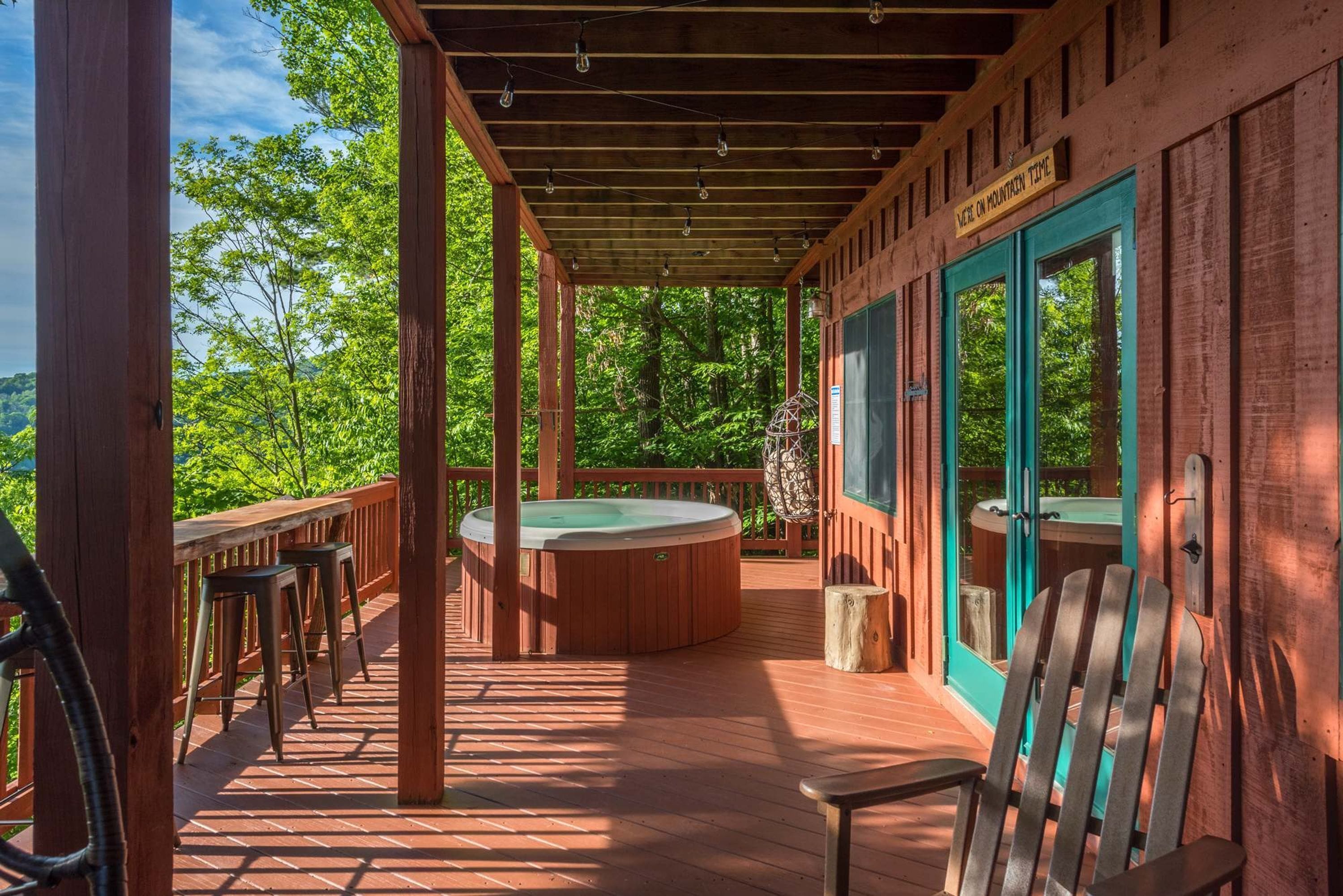 A wooden deck with a hot tub, bar stools, and a covered area with a sign reading 'Motel on Mountain Time.'
