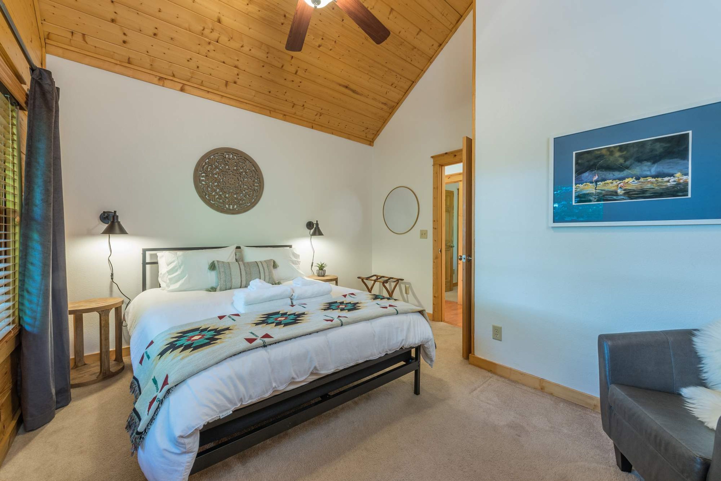 Un dormitorio con cama, mesita de noche, lámpara, reloj de pared, cuadro y puerta que da a otra habitación.