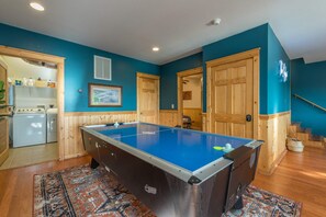 A pool table in a room with teal walls, wooden paneling, and a patterned rug.