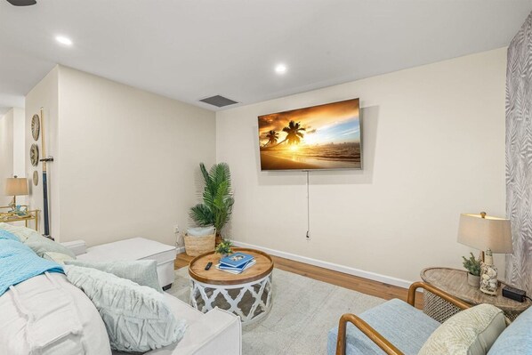 A hotel room with a bed, a round coffee table, a potted plant, a wall-mounted TV, and a lamp. - Beach Bliss Movie Theater Putt Putt Pool (Largo)