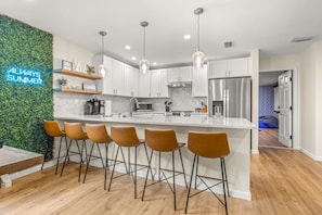 A modern kitchen with white cabinets, stainless steel appliances, and a bar area with stools. - Beach Bliss Movie Theater Putt Putt Pool (Largo)