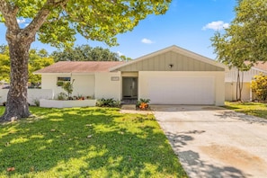 A single-story house with a garage, a well-maintained lawn, and a tree in the foreground. - Beach Bliss Movie Theater Putt Putt Pool (Largo)