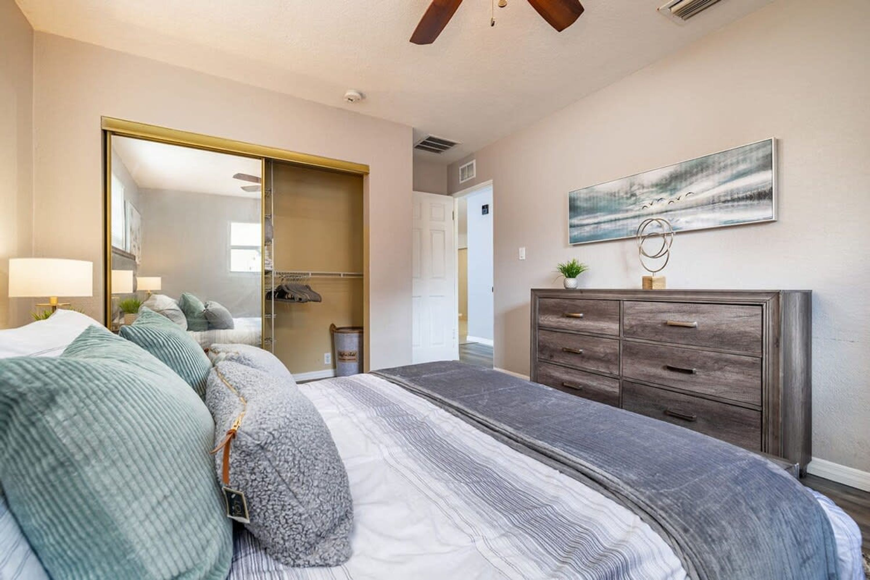 Ein Schlafzimmer mit einem Bett, einem Schminktisch, einem Spiegel und einem Bild an der Wand.