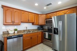 A kitchen with wooden cabinets, stainless steel appliances, a dishwasher, and a granite countertop. - Monthly Rental Comfy Beds Great for Remote Work (Clearwater)