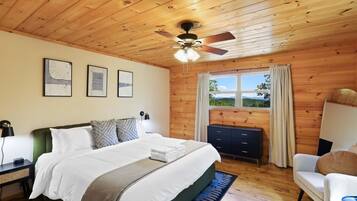 A wooden-paneled bedroom with a bed, a desk, a chair, a ceiling fan, and a window with a view.