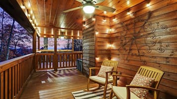 Une terrasse en bois avec un ventilateur de plafond, deux fauteuils à bascule et un mur décoratif.
