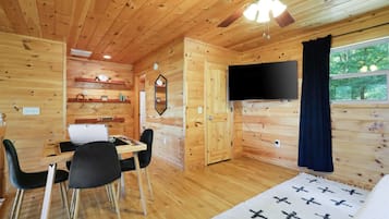 L’intérieur d’un chalet en bois comprend un coin repas, un téléviseur et une fenêtre donnant sur la forêt.