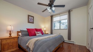 A bedroom with a bed, nightstands, a ceiling fan, a window with curtains, and a door. - The Ridge House Golf Skiing and Hiking (Angel Fire)