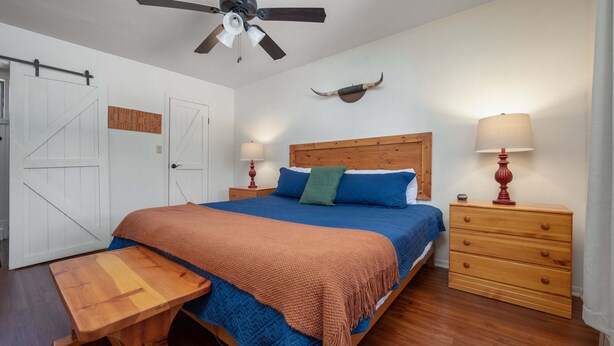 Un dormitorio con una cama, una mesita de noche de madera, un escritorio, un ventilador de techo y un cuerno de toro montado en la pared.