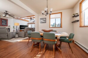 A dining area with a wooden table and chairs, a ceiling fan, and a window with blinds. - The Ridge House Golf Skiing and Hiking (Angel Fire)