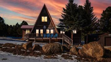 A wooden cabin with a triangular roof, a porch with blue railings, and a view of the surrounding forest.