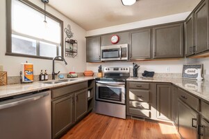 Cocina con electrodomésticos de acero inoxidable, armarios de madera, una ventana y un reloj en la pared.