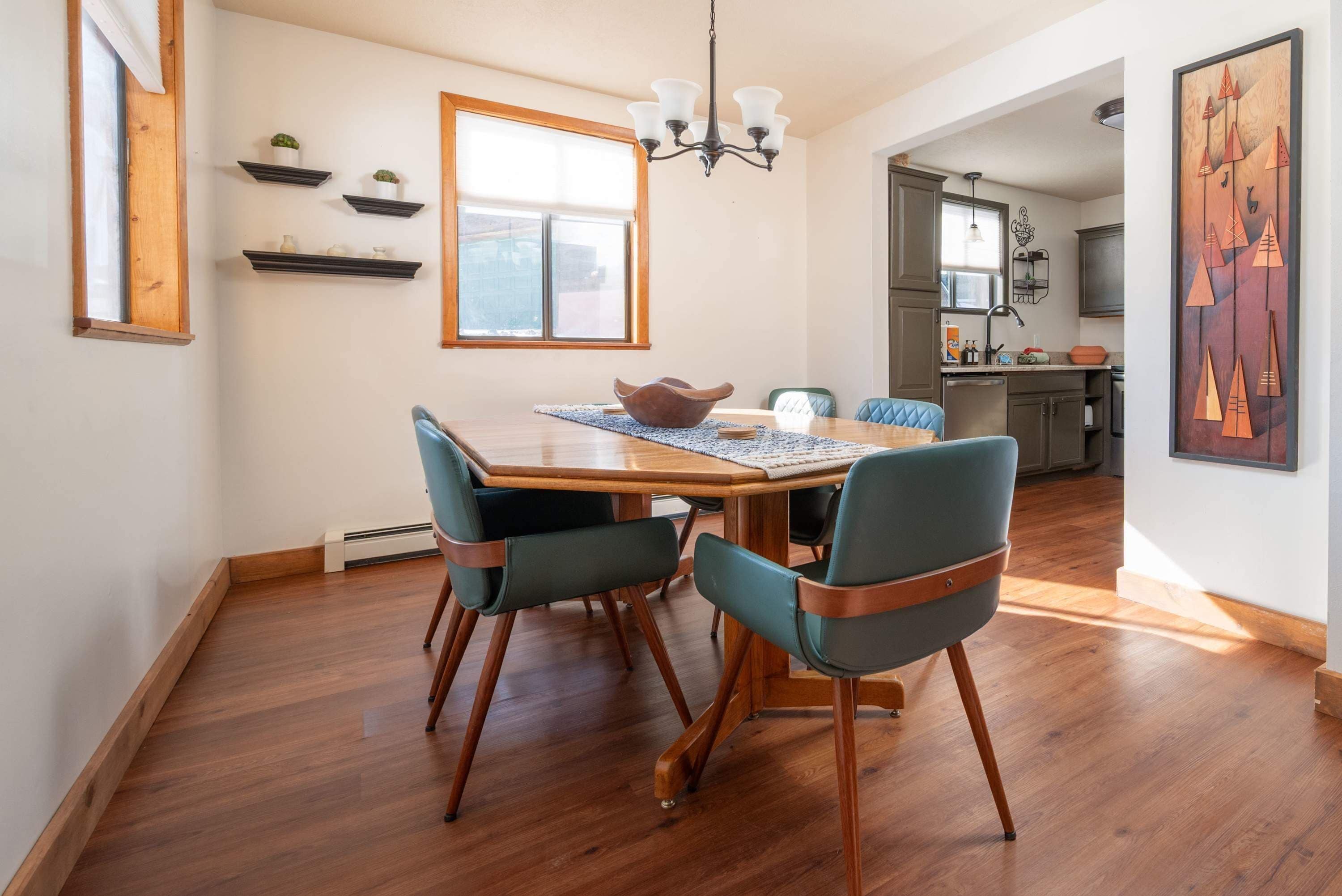 A dining area with a wooden table, two chairs, a chandelier, and a window.