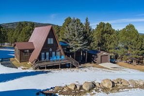 A cabin with a sloped roof, a porch with chairs, and a small shed. - The Ridge House Golf Skiing and Hiking (Angel Fire)