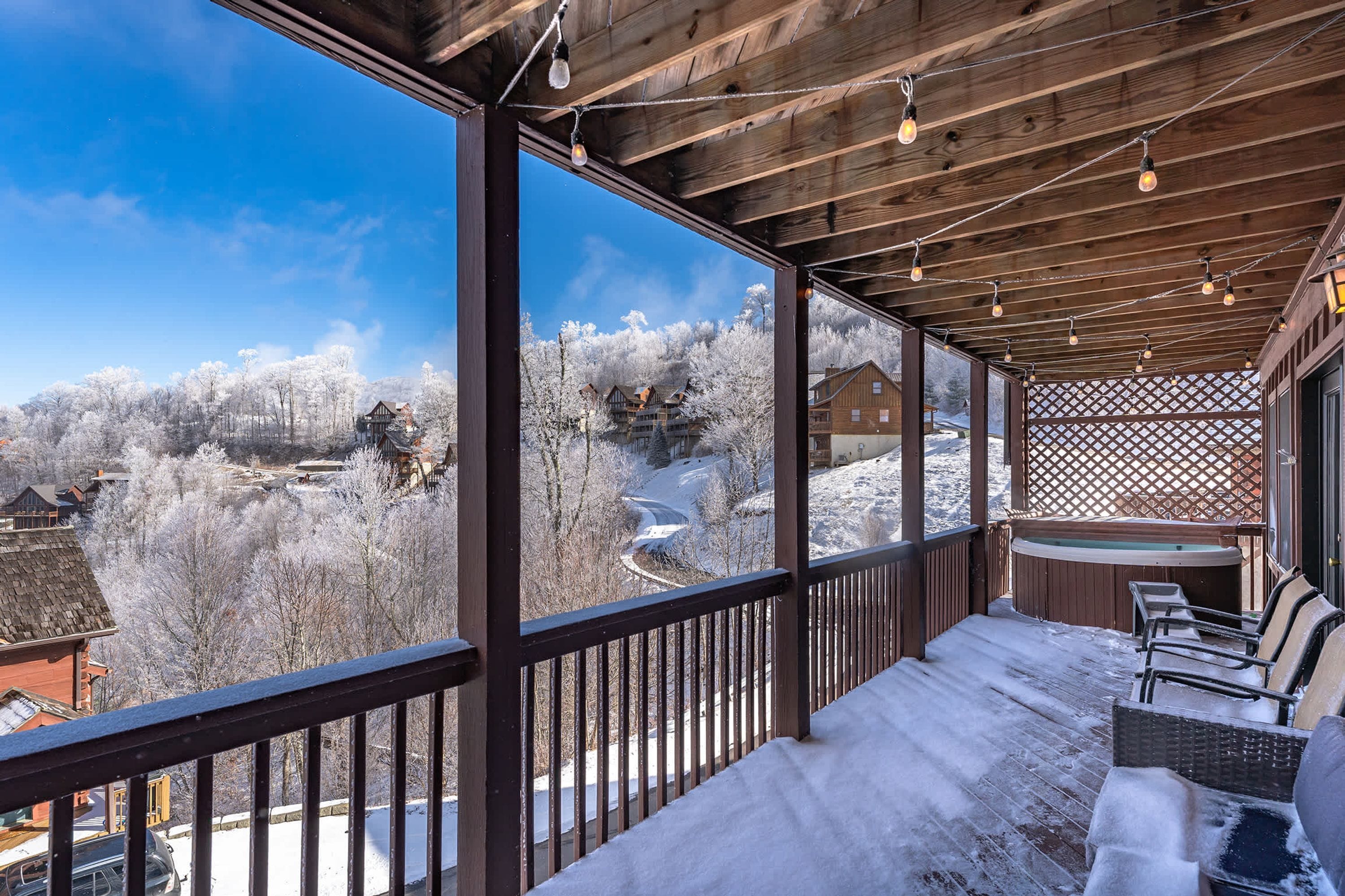 A wooden deck with a snow-covered ground, a seating area with a bench and chairs, and a view of a snowy landscape with buildings.