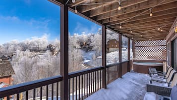 A wooden deck with a snow-covered ground, a seating area with a bench and chairs, and a view of a snowy landscape with buildings.