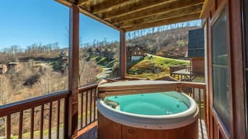 A wooden deck with a hot tub, overlooking a hilly landscape with houses.