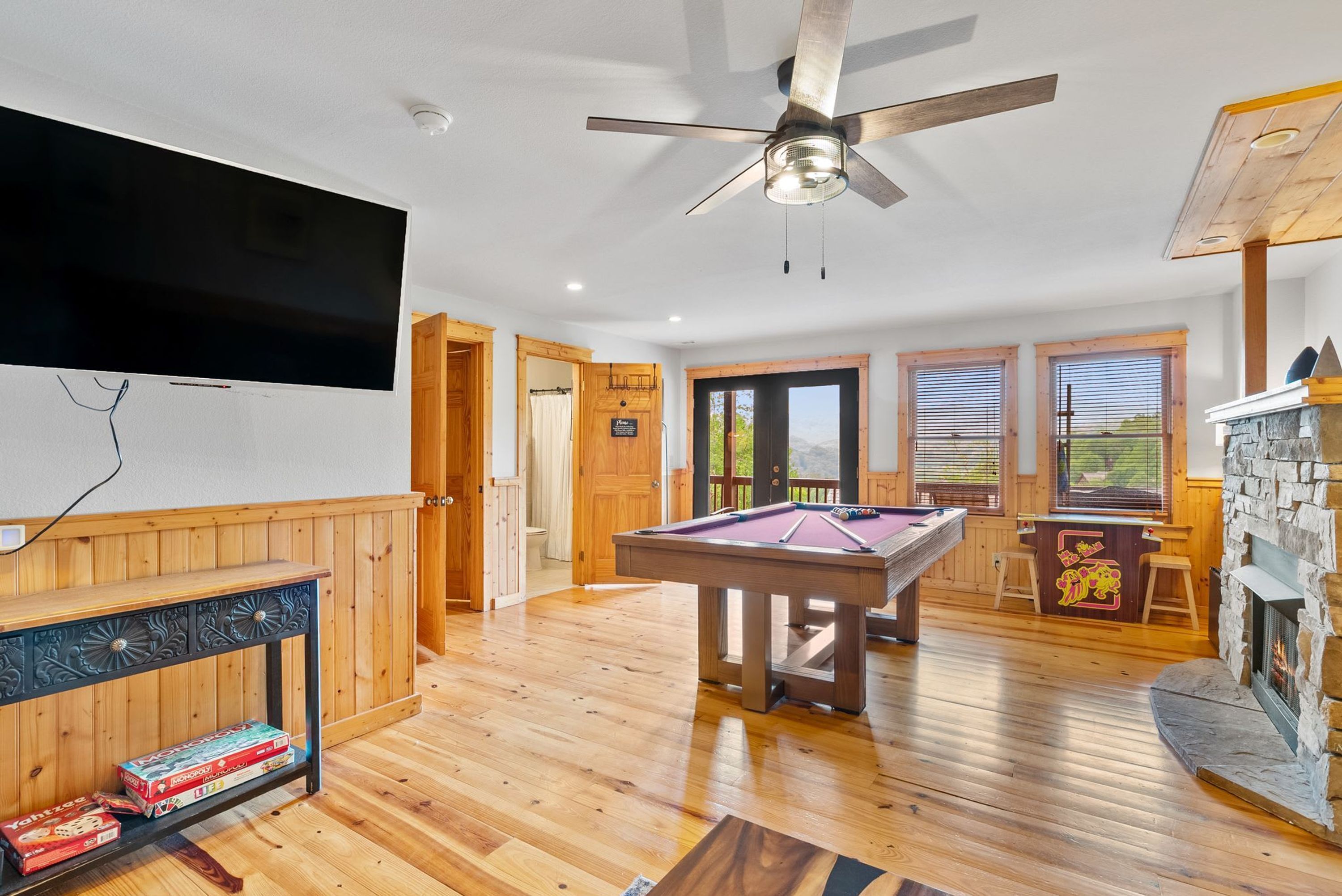 Quarto com mesa de bilhar, lareira, televisão na parede e piso de madeira.