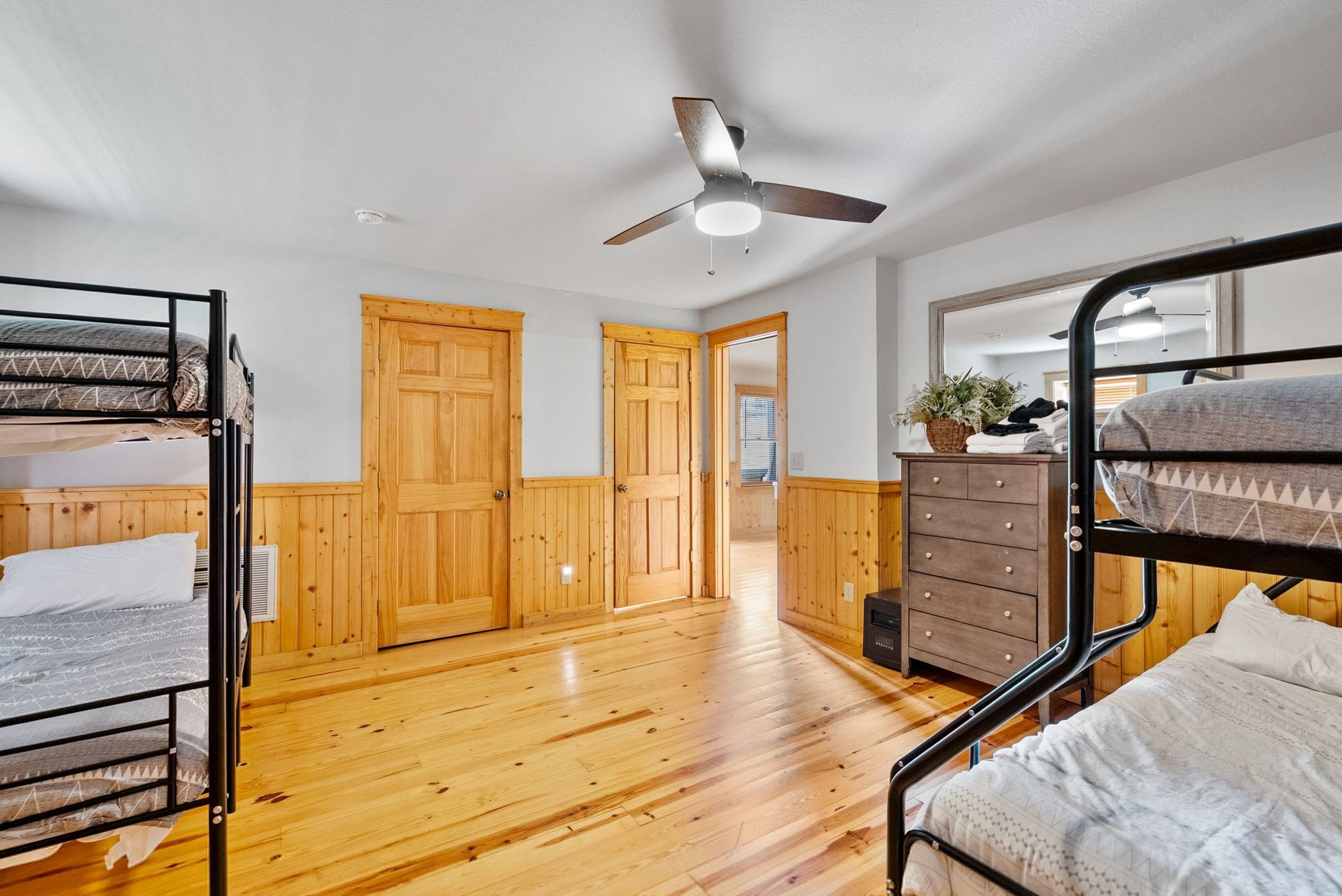 A room with bunk beds, wooden doors, a ceiling fan, and a dresser with a mirror.
