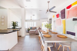 A spacious kitchen with a dining area, featuring a long table with woven placemats, a ceiling fan, and a modern design. - Right Near Old Town 4BR With Heated Pool (Scottsdale)