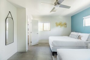 A bedroom with two beds, a ceiling fan, a wall-mounted light fixture, and a door leading to another room. - Right Near Old Town 4BR With Heated Pool (Scottsdale)