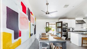 A modern kitchen with a dining area, featuring a ceiling fan, white cabinetry, and a large abstract painting on the wall. - Right Near Old Town 4BR With Heated Pool (Scottsdale)