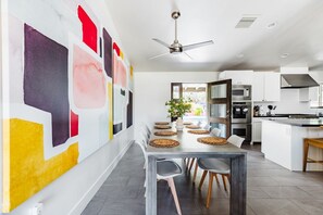 A modern kitchen with a dining area, featuring a ceiling fan, white cabinetry, and a large abstract painting on the wall. - Right Near Old Town 4BR With Heated Pool (Scottsdale)