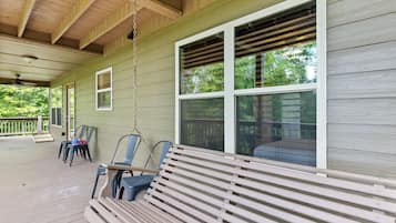 Une véranda avec un banc en bois, des chaises et une balançoire.