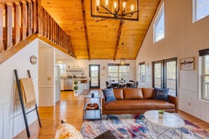 A spacious living room with a wooden staircase, a brown leather sofa, and a dining area with a view. - Valley Retreat Sleeps 10 Hot Tub Fire Pit (Blue Ridge)