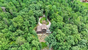 A cabin surrounded by dense forest, with a driveway leading to the entrance.